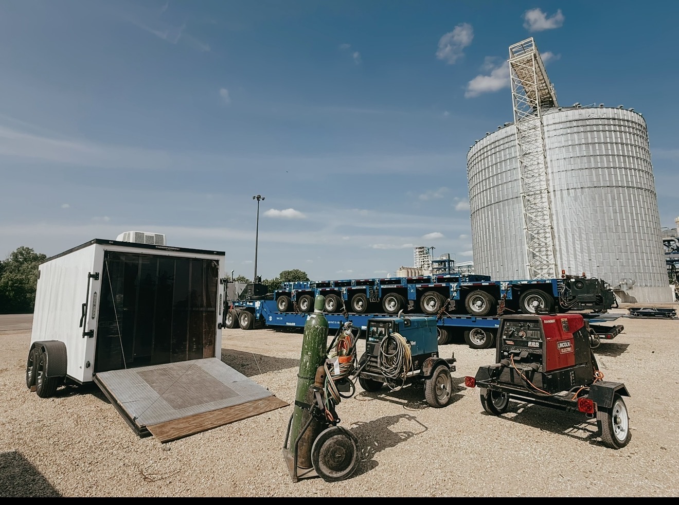 Heavy-haul trailers and welding equipment staged near an industrial silo
